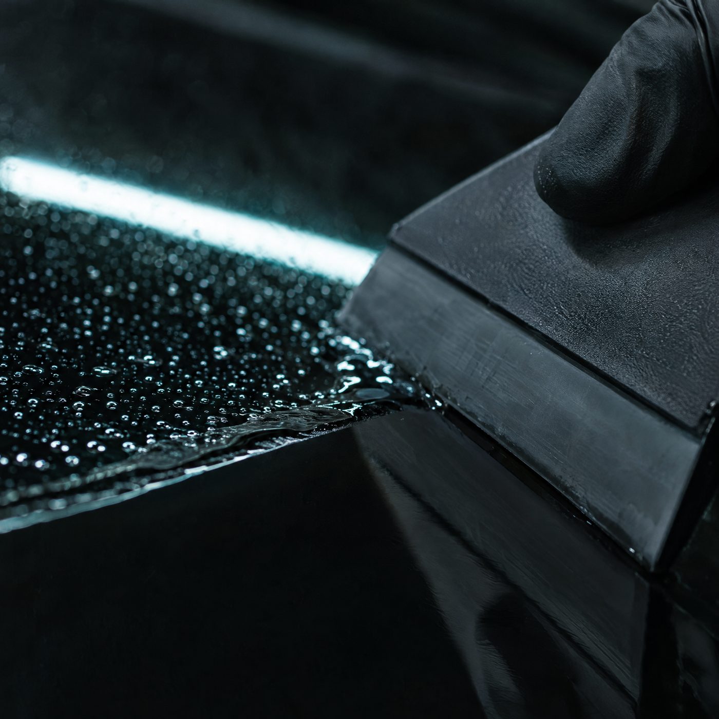 Macro close-up of a squeegee pushing the last water out from under fresh dark tint film